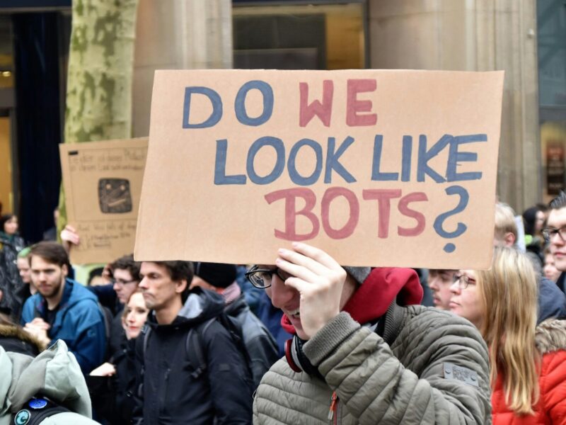 Image d'une manifestation où un homme tient une pancart avec écrit en anglais " Do we like bots? "